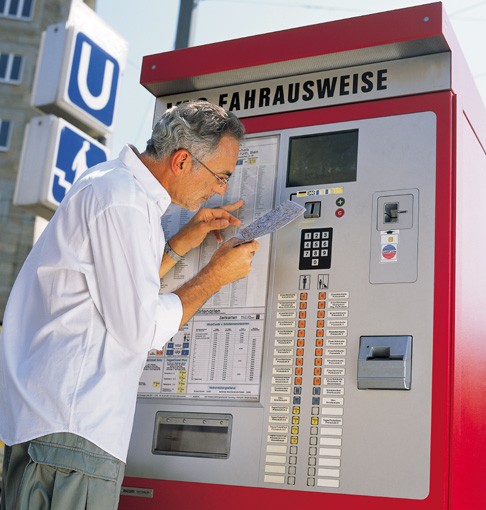 Mann wendet die monokulare Lupenbrille am Ticketautomat an