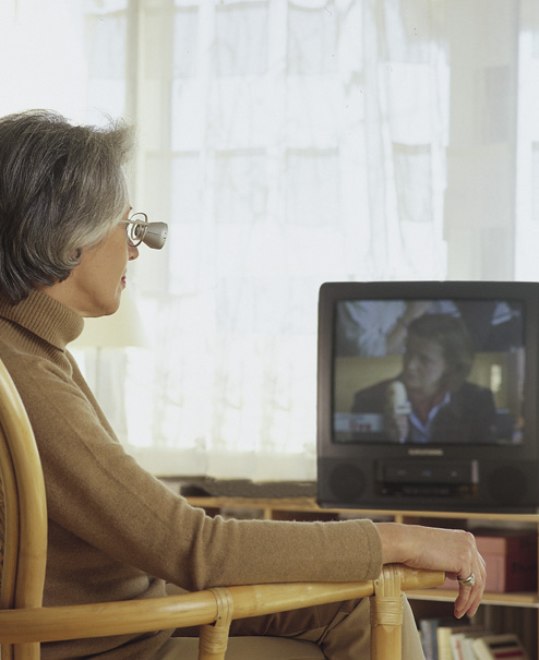 Dame schaut mit einer Fernrohrlupenbrille in den Fernseher