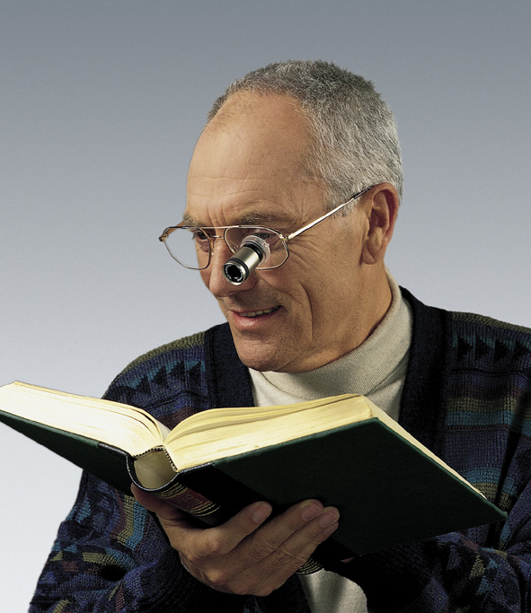Mann liest mit einer Fernrohrbrille ein Buch